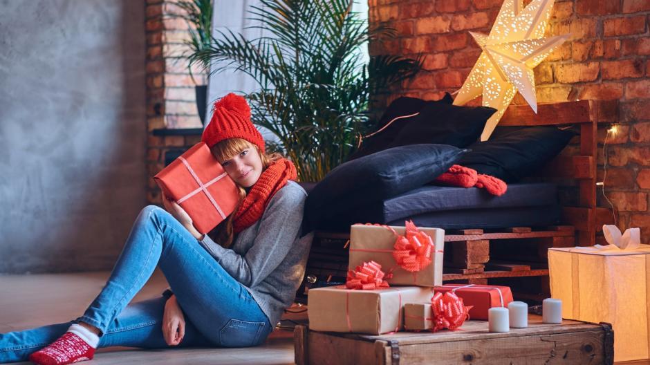 femme assise enlaçant un cadeau de Noël, entourée de paquets sous le sapin