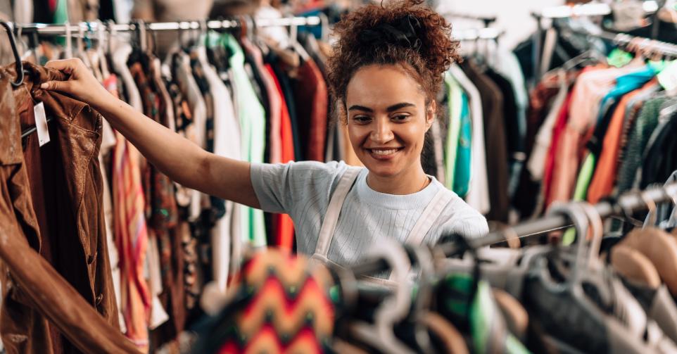 Young woman smiling while browsing through clothes in a second-hand shop, embracing sustainable fashion and promoting a zero-waste lifestyle with each thoughtful choice