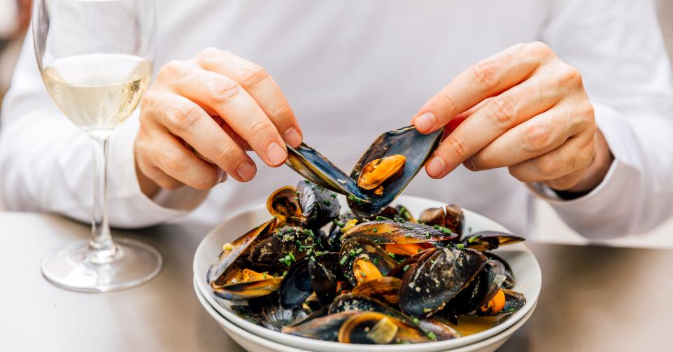 Man eating mussels with white wine in a seafood restaurant, close-up view