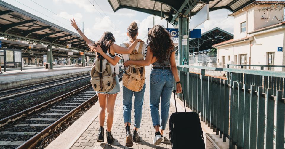 Three friends enjoying a trip together - Rear view. They are at a railroad train station.
