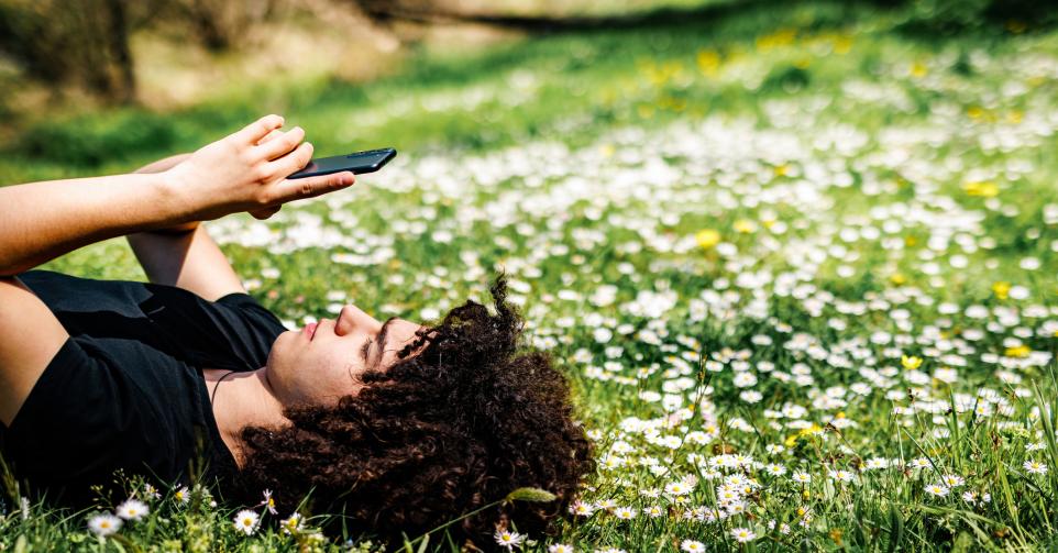 Teenage boy surfing the net while lying down on grass at springtime