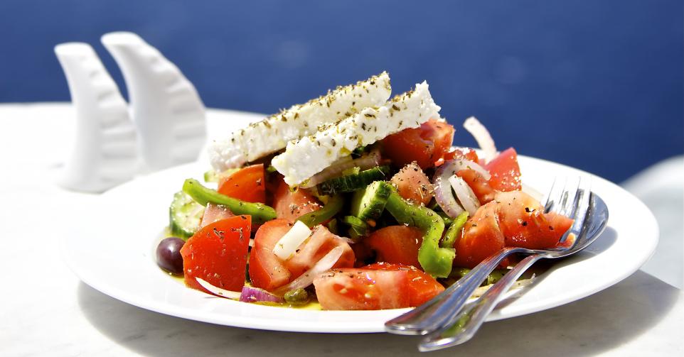 Greek salad on white plate in front of sea.