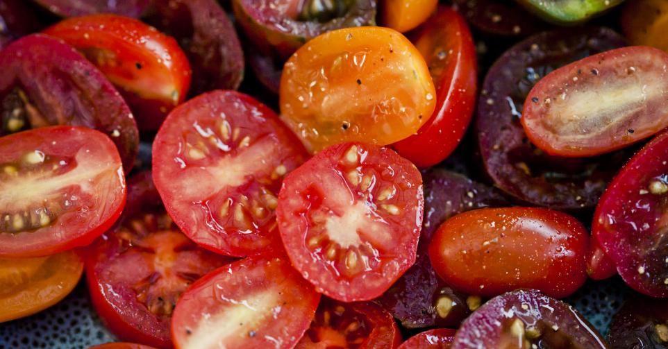 Close-up of a bowl of halved cherry tomatoes seasoned with pepper.
