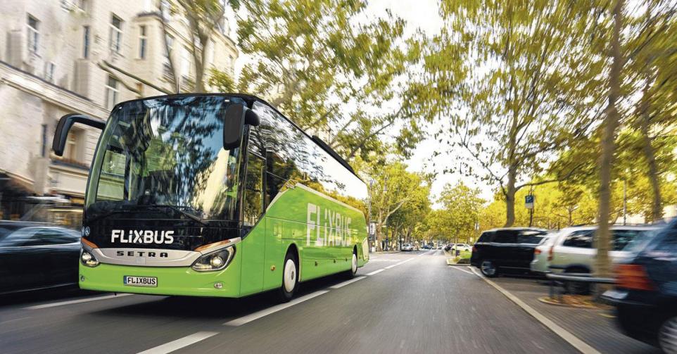 Un des bus verts de FlixBus roulant dans une rue arborée