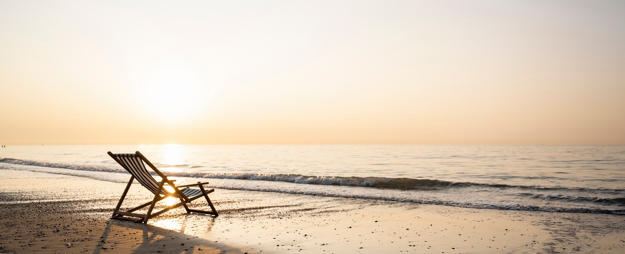 Empty folding chair on shore at beach against clear sky during sunset