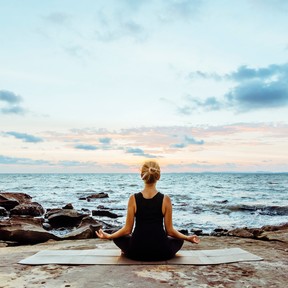 Young woman performs yoga moves on bluff above sea