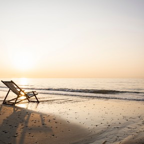Empty folding chair on shore at beach against clear sky during sunset