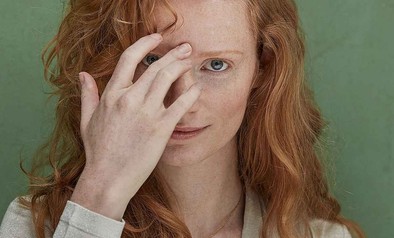 Vrouw met rode haren poseert voor een groene muur